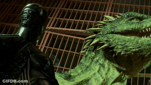 A Statue Of A Man Standing Next To A Large Green Monster GIF