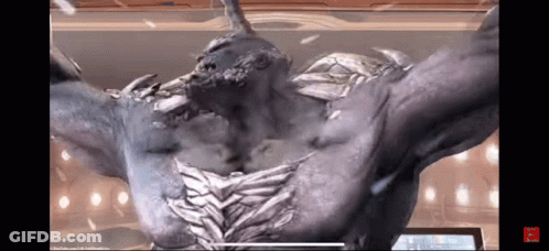 A Statue Of A Monster With Horns And Wings Is Standing In Front Of A Screen . GIF