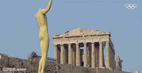 A Statue Of A Naked Man Stands In Front Of A Building With The Olympic Rings On The Bottom GIF