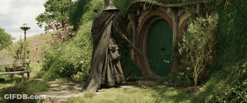 A Statue Of A Wizard Standing In Front Of A Hobbit House GIF
