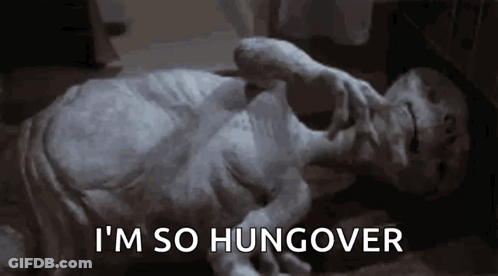 A Statue Of An Alien Is Laying On The Floor With The Words `` I 'M So Hungover '' Written On The Bottom . GIF