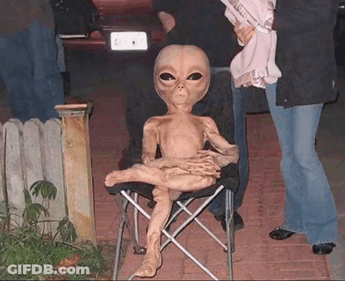 A Statue Of An Alien Is Sitting In A Chair With A License Plate That Says A1 GIF
