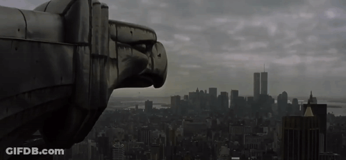 A Statue Of An Eagle Looks Out Over A City With The Twin Towers In The Background GIF