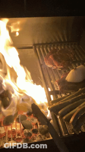A Steak Is Being Cooked On A Grill With Flames Behind It GIF