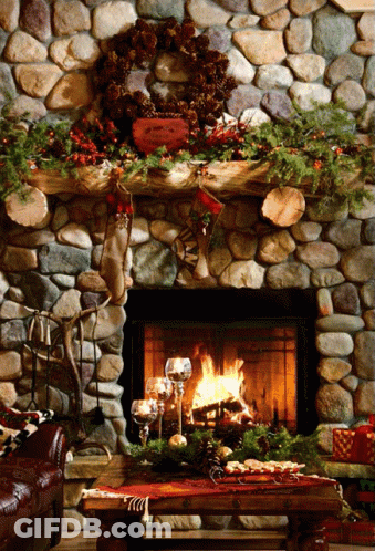 A Stone Fireplace Decorated For Christmas With A Wreath And Stockings On The Mantle GIF