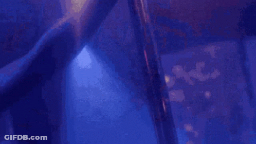 A Stripper Is Dancing On A Pole In A Dark Room With Purple Lights . GIF
