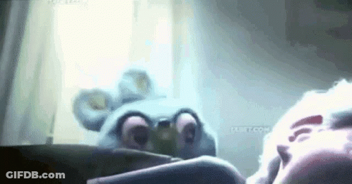 A Stuffed Animal Is Laying On A Bed Next To A Person In A Room . GIF