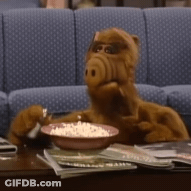 A Stuffed Animal Is Sitting At A Table With A Bowl Of Popcorn GIF