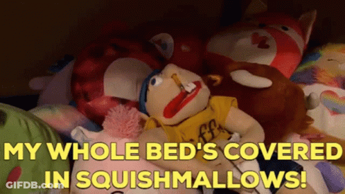A Stuffed Animal Laying On A Bed With The Words " My Whole Bed 'S Covered In Squishmallows ! " GIF