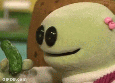 A Stuffed Animal With A Pink Bow On Its Head Is Holding A Green Pickle . GIF