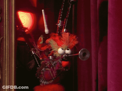 A Stuffed Animal With Big Eyes Is Holding A Bagpipe In Front Of A Red Curtain GIF