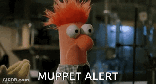A Stuffed Animal With Red Hair And Big Eyes Is Standing In Front Of A Banana And Says `` Muppet Alert '' . GIF