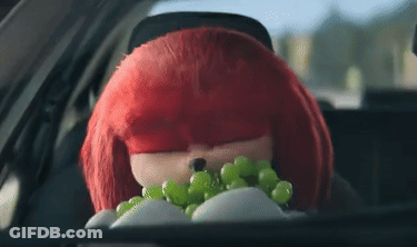 A Stuffed Animal With Red Hair Is Sitting In A Car Holding A Bunch Of Green Grapes . GIF