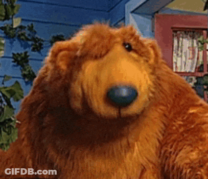 A Stuffed Bear With A Blue Nose Is Standing In Front Of A Blue House GIF