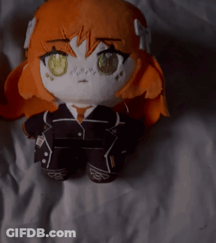 A Stuffed Doll With Orange Hair And Yellow Eyes Is Laying On A White Sheet GIF