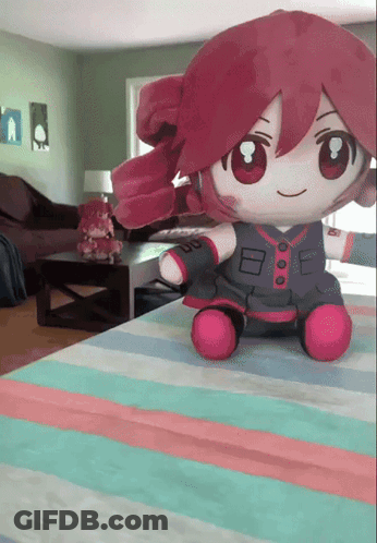 A Stuffed Doll With Red Hair Is Sitting On A Striped Blanket GIF