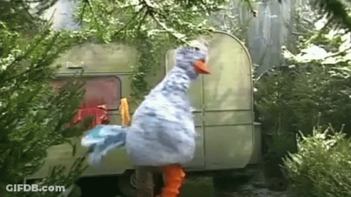 A Stuffed Duck Is Standing In Front Of A Trailer In A Forest . GIF