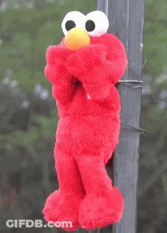 A Stuffed Elmo With A Yellow Hat Is Hanging On A Pole GIF