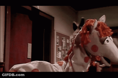 A Stuffed Horse With A Red Mane And Tail Is Standing In A Hallway GIF