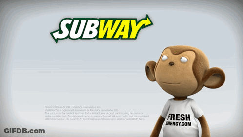 A Stuffed Monkey Is Standing In Front Of A Subway Ad GIF