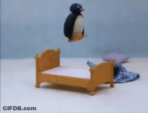 A Stuffed Penguin Is Flying Over A Small Wooden Bed GIF