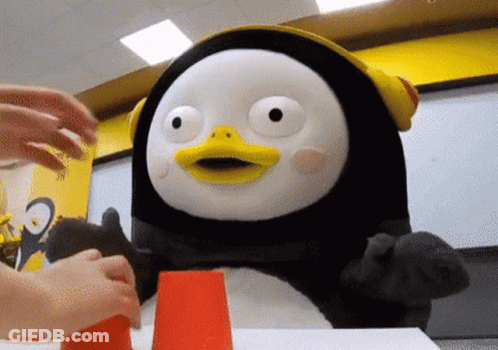 A Stuffed Penguin Wearing Headphones Is Sitting At A Table With A Person Playing With It . GIF