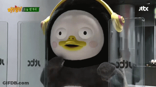 A Stuffed Penguin Wearing Headphones Stands In Front Of A Sign That Says Jtcc GIF