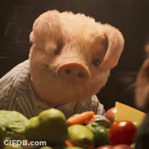 A Stuffed Pig Wearing A Striped Shirt Is Sitting In Front Of A Bowl Of Fruits And Vegetables GIF