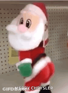 A Stuffed Santa Claus Is Standing In Front Of A Shelf And Holding A Christmas Ball . GIF