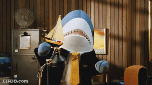 A Stuffed Shark In A Suit And Tie Holds A Small Boat GIF