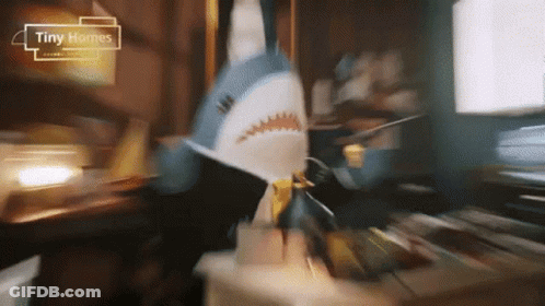 A Stuffed Shark Is Sitting On A Table With Tiny Homes Written On The Bottom GIF