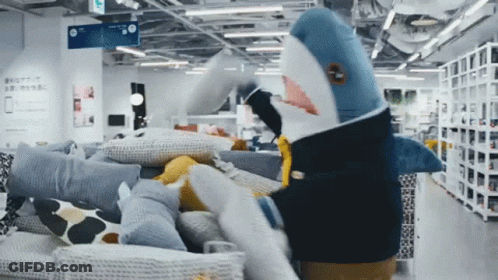 A Stuffed Shark Is Standing In A Store With Pillows GIF