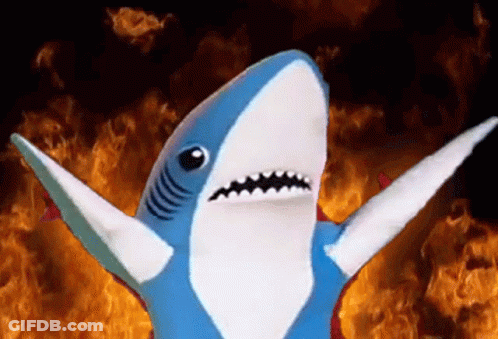 A Stuffed Shark Is Standing In Front Of A Fire GIF