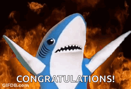 A Stuffed Shark Says Congratulations In Front Of A Fire Background GIF