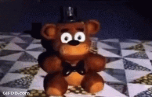 A Stuffed Teddy Bear With Big Eyes And A Bow Tie Is Sitting On A Checkered Table . GIF