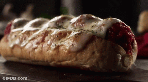 A Sub Sandwich With Meatballs And Cheese On A Table GIF