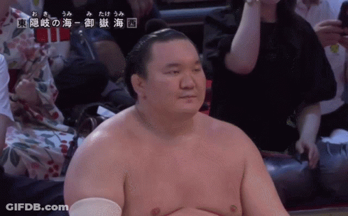 A Sumo Wrestler Is Sitting In A Stadium With Chinese Writing On The Bottom Right GIF