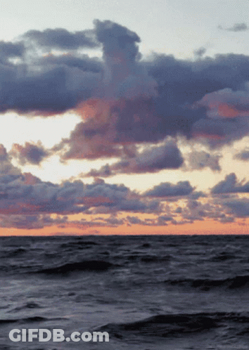 A Sunset Over A Large Body Of Water With Clouds GIF