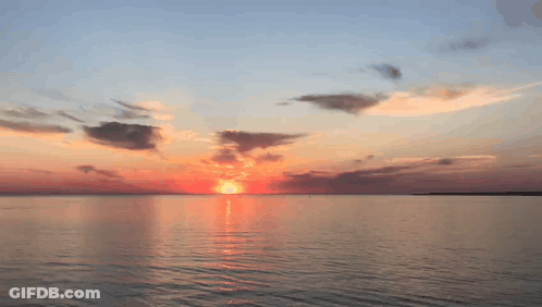 A Sunset Over A Large Body Of Water With The Sun Shining Through The Clouds GIF