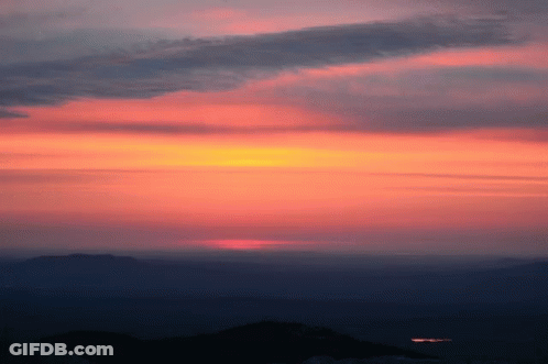 A Sunset With Mountains In The Foreground And A Dark Sky In The Background GIF