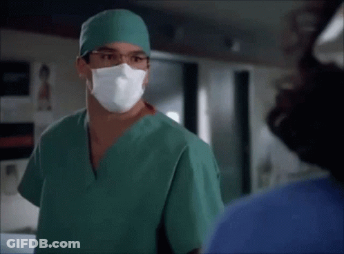 A Surgeon Wearing A Green Scrub And A Mask Talks To A Nurse GIF