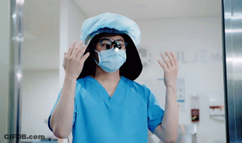 A Surgeon Wearing A Mask And Goggles Stands In Front Of A Sign That Says ' Surgery ' GIF