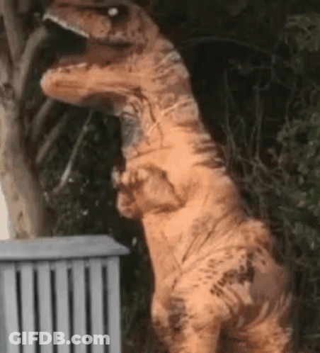 A T-Rex Costume Is Standing Next To A Fence . GIF