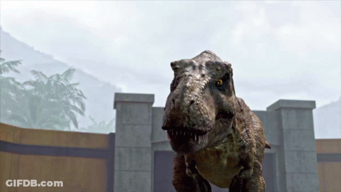 A T-Rex Is Standing In Front Of A Stone Wall GIF