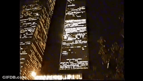 A Tall Building Is Lit Up At Night With A Street Light In The Foreground GIF