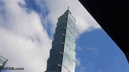 A Tall Building With A Blue Sky And Clouds In The Background GIF