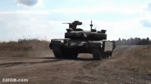 A Tank Is Driving Down A Dirt Road In A Field . GIF