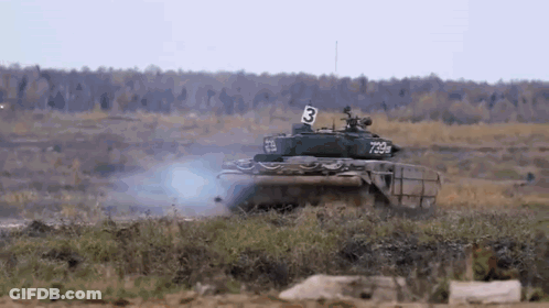A Tank With The Number 3 On The Side Is Driving Through A Grassy Field . GIF