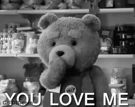 A Teddy Bear Is Holding A Sign That Says `` You Love Me '' In A Black And White Photo . GIF