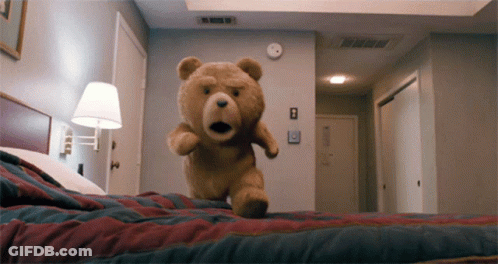 A Teddy Bear Is Jumping On A Bed In A Bedroom GIF